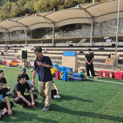 잔디 운동장에서 마이크를 들고 참가자들에게 안내하는 진행자