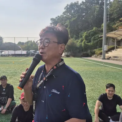잔디 운동장에서 마이크를 들고 참가자들에게 안내하는 진행자