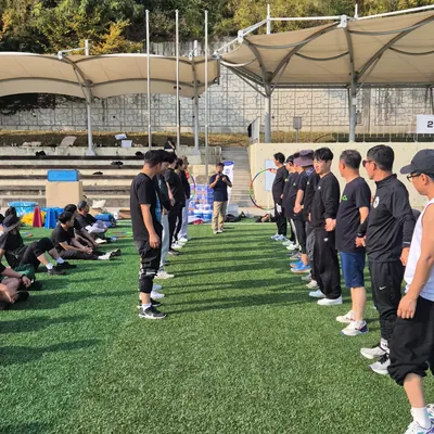 야외 운동장에서 진행자의 안내에 따라 팀 게임을 하는 참가자들