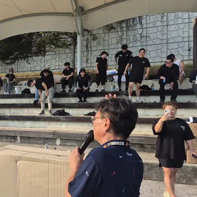 잔디 운동장에서 마이크를 들고 참가자들에게 안내하는 진행자